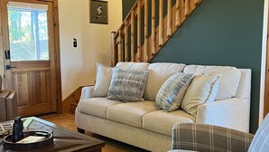 Una sala de estar acogedora con una escalera de madera, un sofá, un sillón escocés y una mesa de centro.