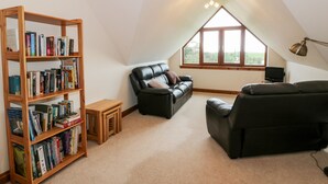 A cozy attic room with a black leather sofa, a wooden bookshelf, and a small table. - Cairnhapple House (Stranraer)