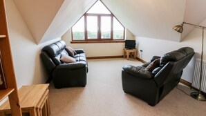 A cozy attic room with two leather recliners, a wooden table, and a TV on a small stand. - Cairnhapple House (Stranraer)