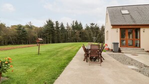 A building with a wooden door and windows, a concrete pathway, and a grassy area with a bird feeder. - Cairnhapple House (Stranraer)