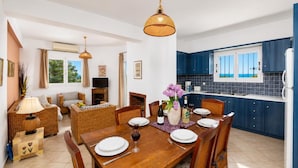 A dining area with a wooden table set for six, surrounded by wicker chairs. - Villa Thalia Katerina (Mousata)