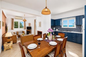 A dining area with a wooden table set for six, surrounded by wicker chairs. - Villa Thalia Katerina (Mousata)