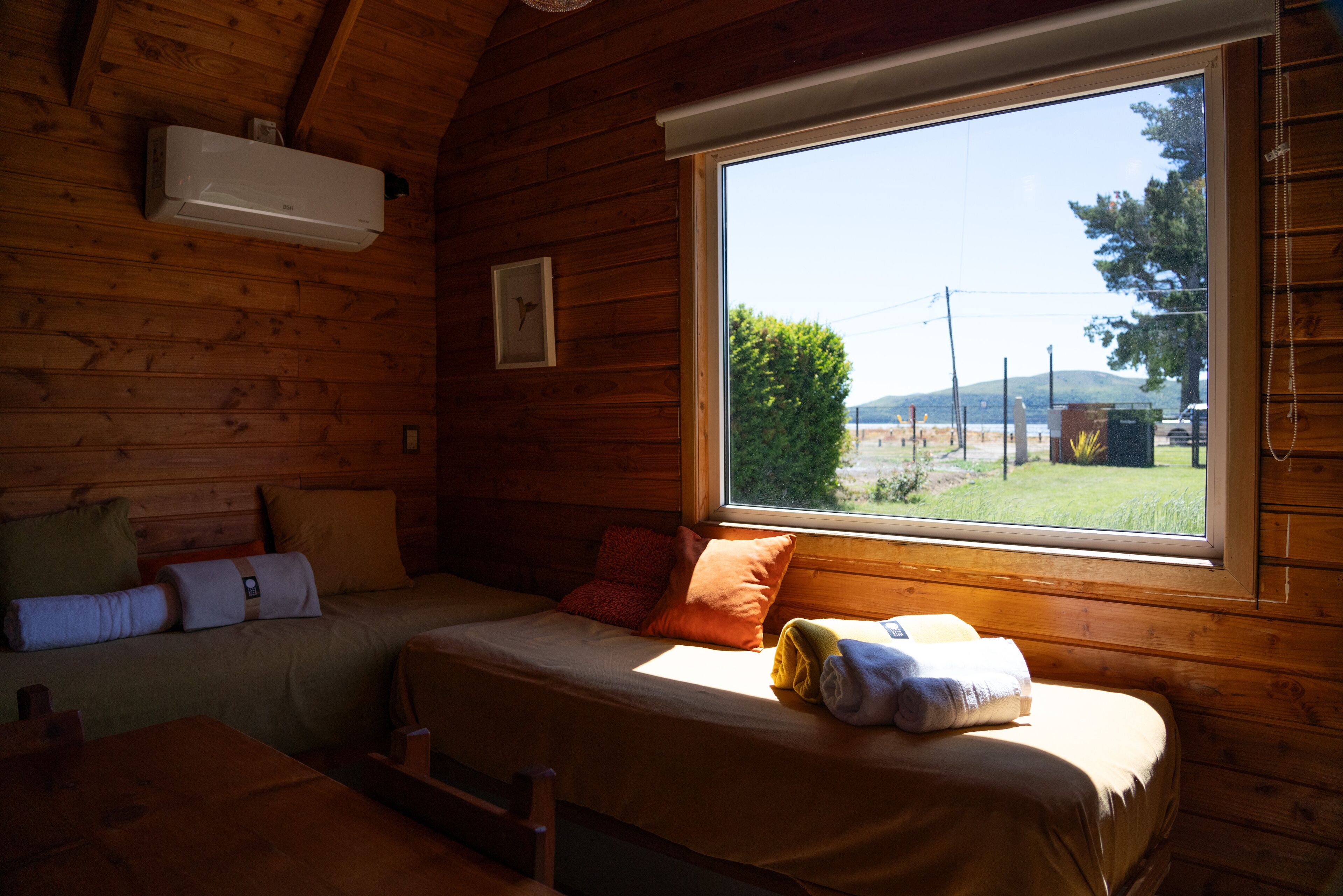 A cozy cabin room with a bed, a window with a view of the outdoors, and a wall-mounted air conditioner.