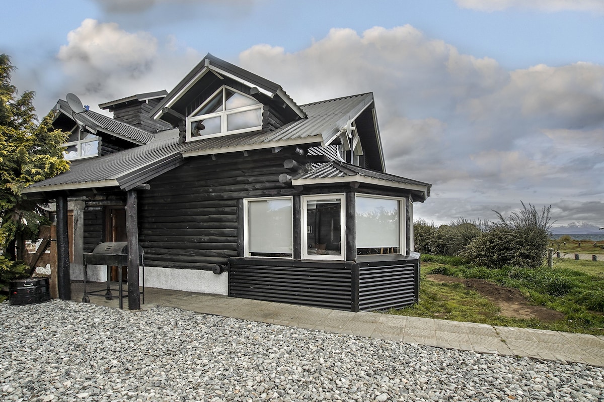Une cabane en rondins avec un toit en pente, de grandes fenêtres et une allée gravillonnée.