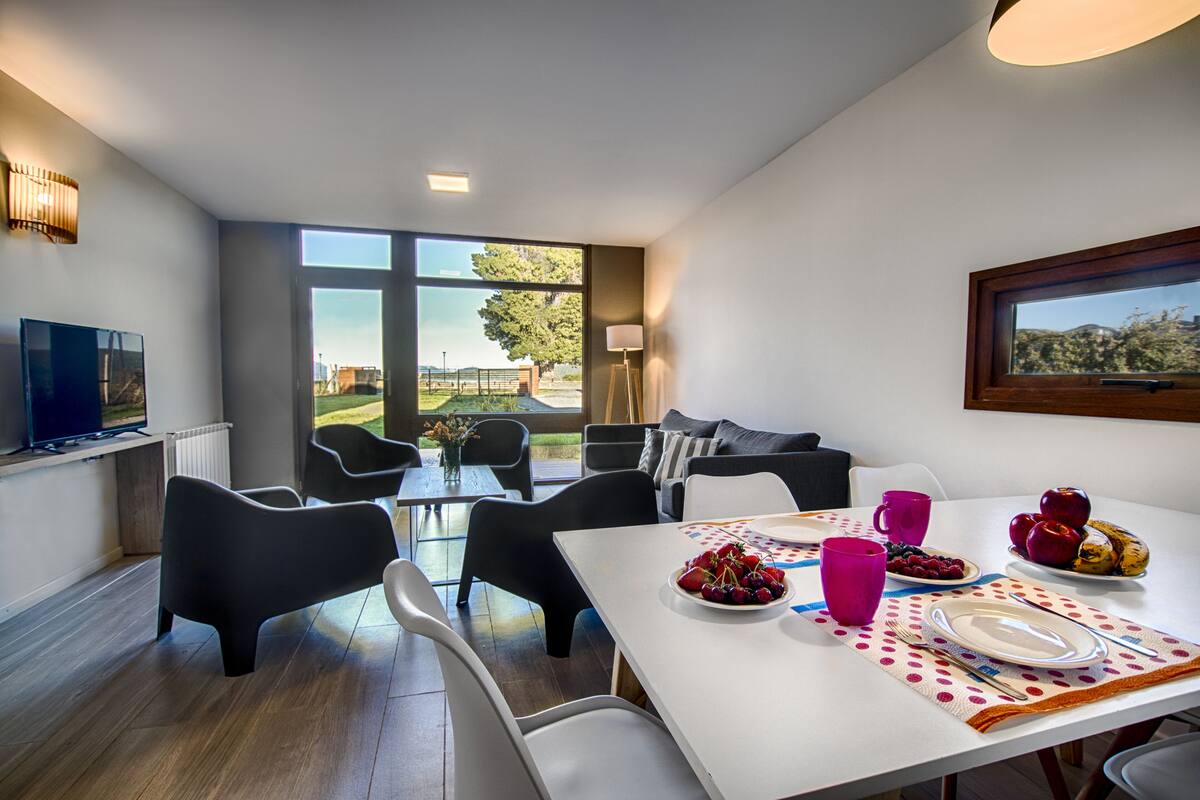Un comedor moderno con una mesa dispuesta para dos personas, un televisor y vistas al exterior.