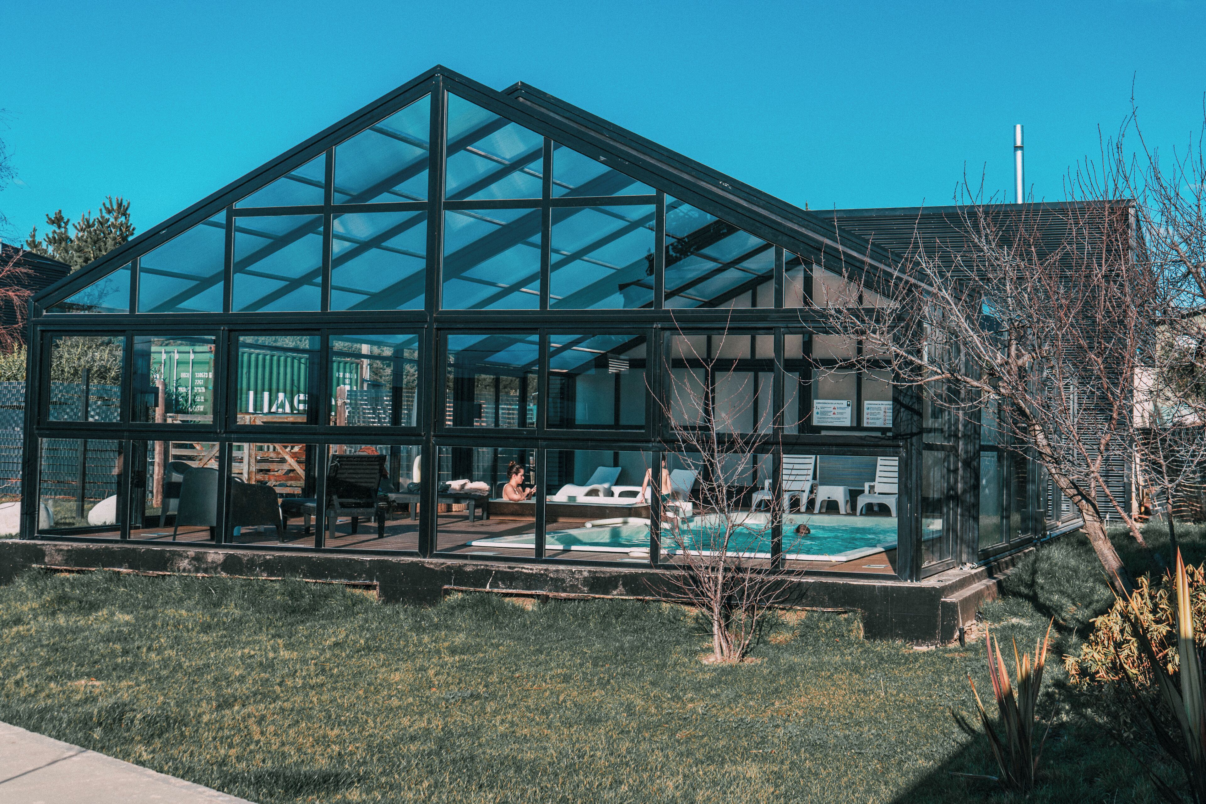 Une maison moderne en verre avec une piscine, dotée d’un toit transparent et offrant une vue sur les environs.