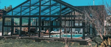Une maison moderne en verre avec une piscine, dotée d’un toit transparent et offrant une vue sur les environs.