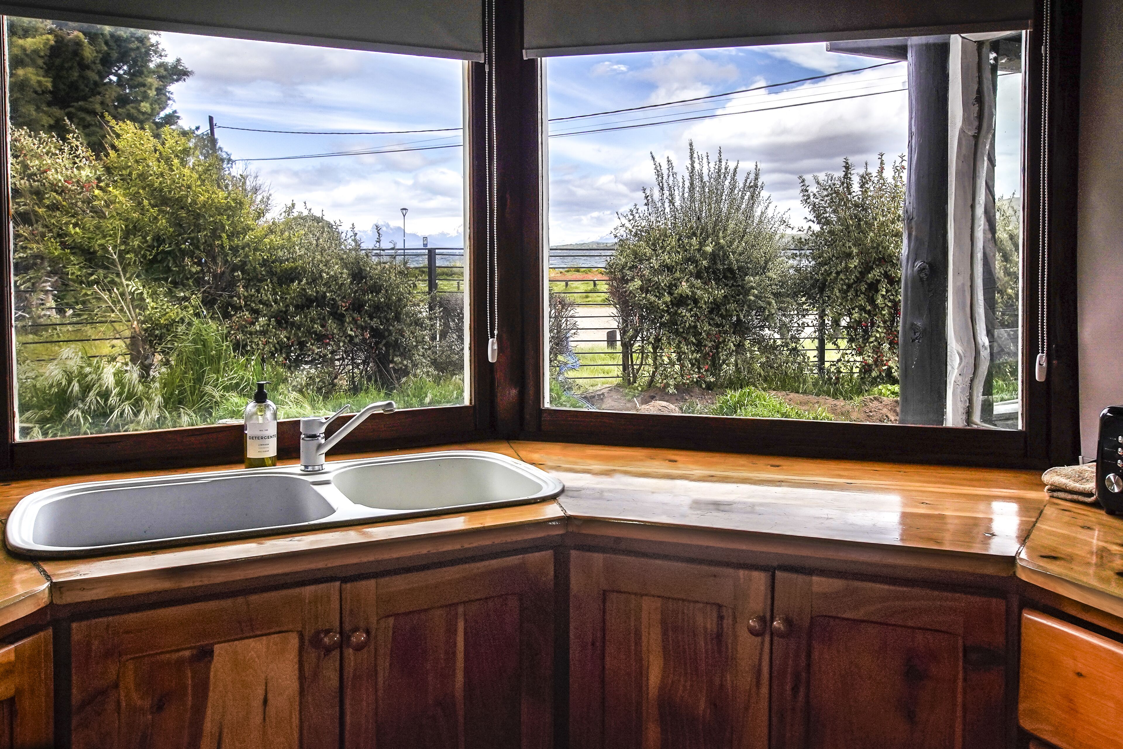 A kitchen with a large window, wooden cabinets, and a double sink.