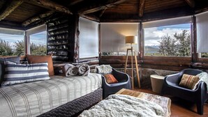 Interior acogedor de una cabaña con una cama, dos sillones, una lámpara y vistas al exterior.