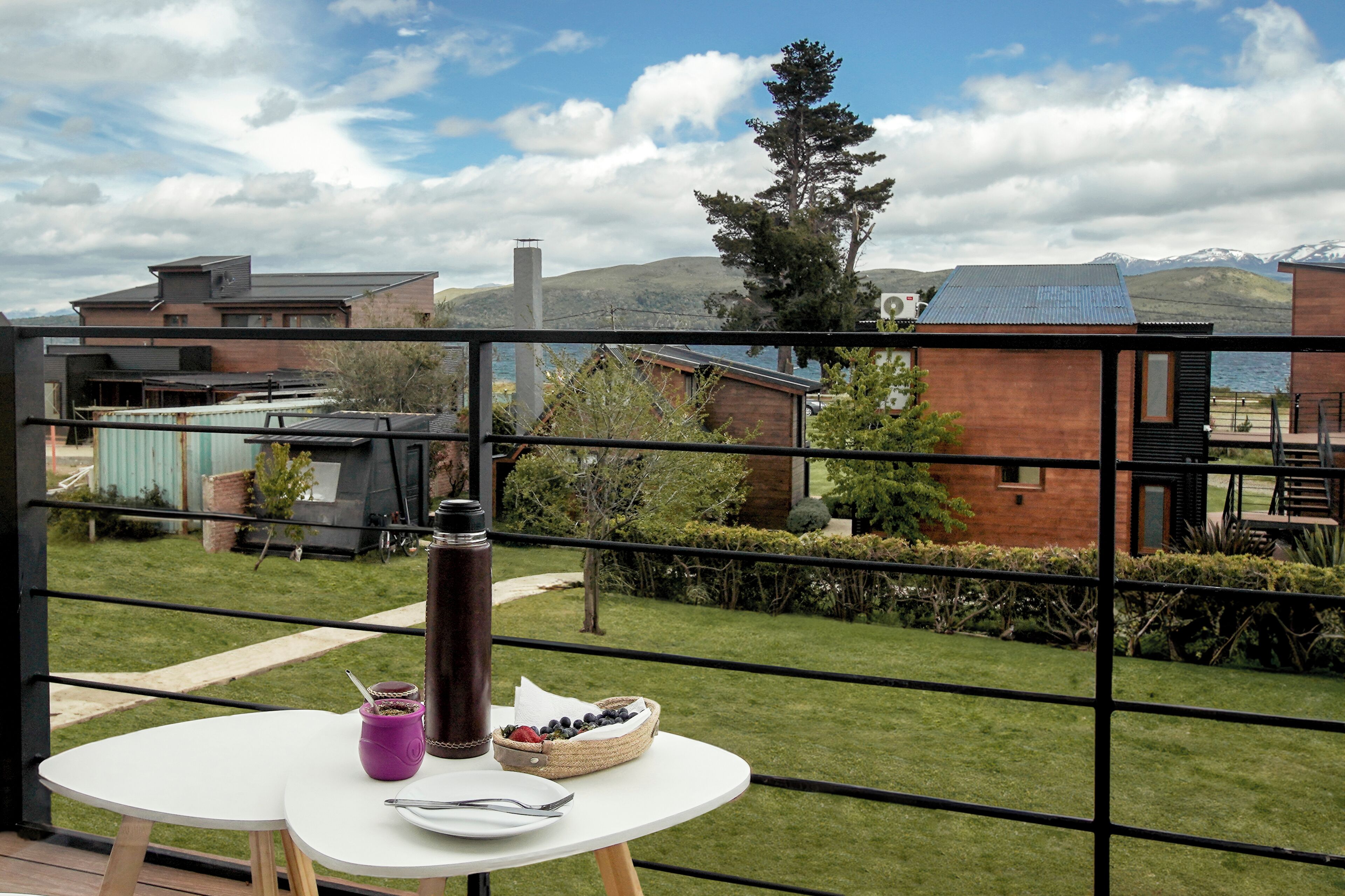 Un balcon avec une table dressée pour deux personnes, donnant sur un quartier résidentiel avec des maisons et une montagne visible au loin.