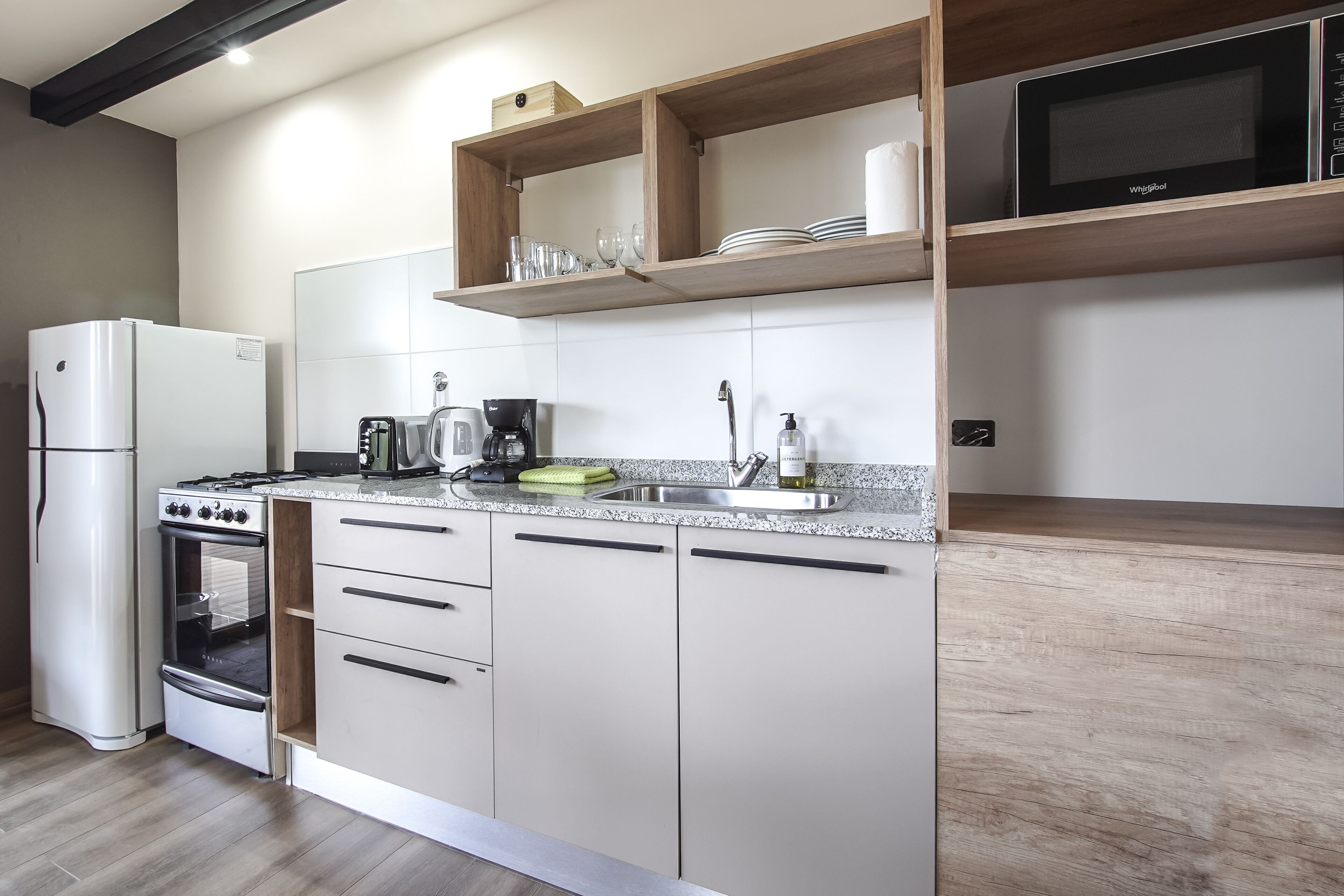 Una cocina moderna con horno empotrado, cafetera y estantes de madera sobre la encimera.