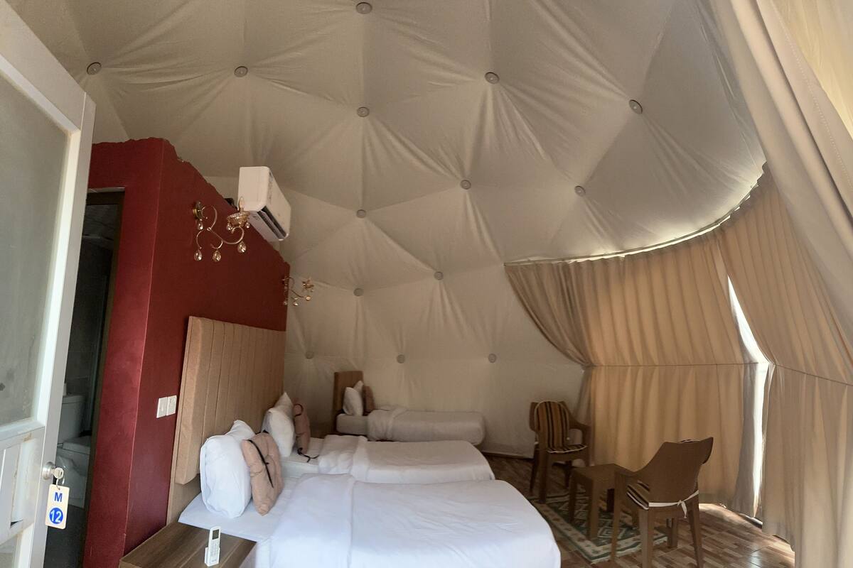 Een ruime tent met een groot bed, een houten stoel en een kleine tafel.