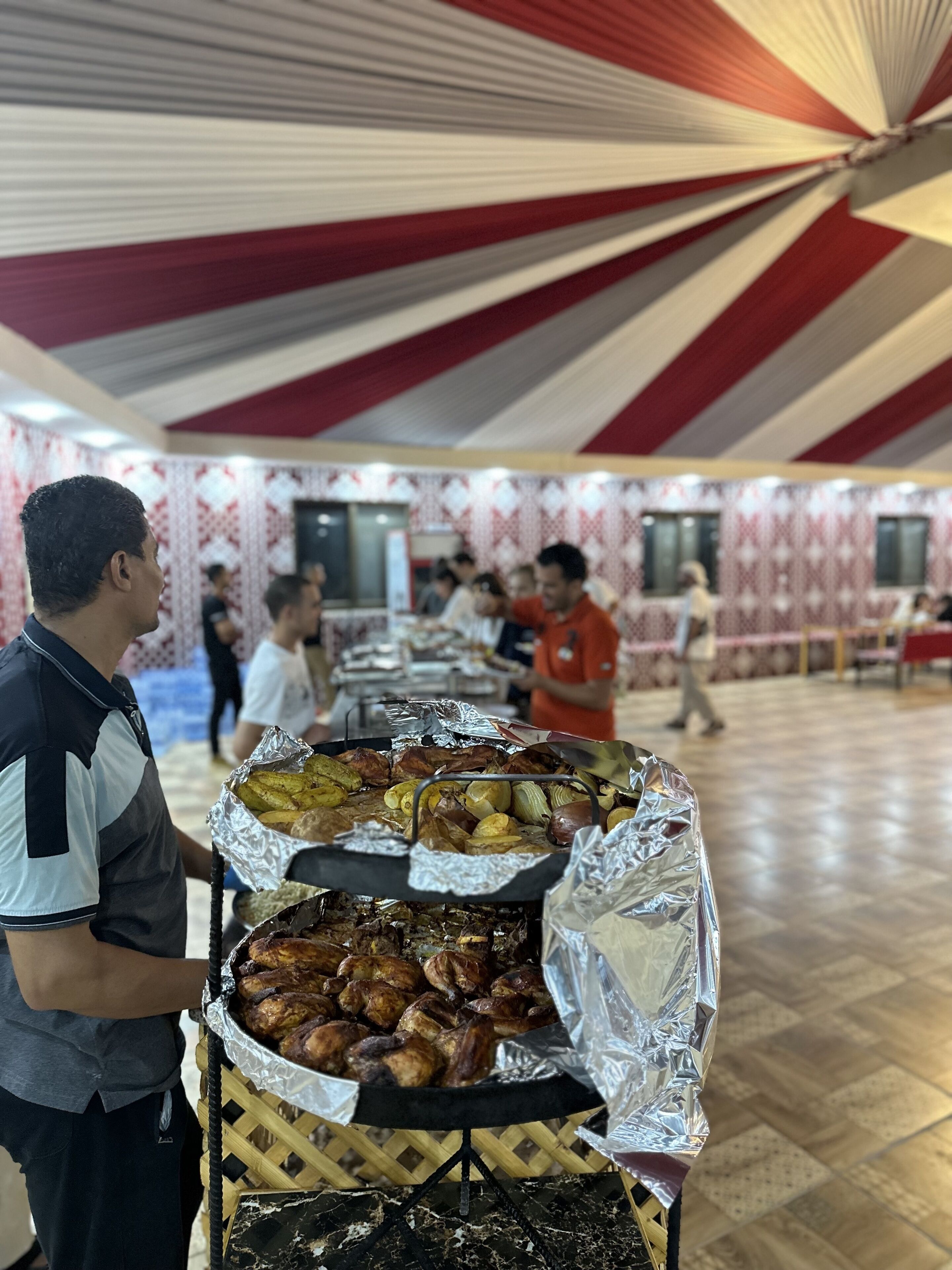 A buffet setup with various dishes covered in foil, a grill, and a patterned ceiling.
