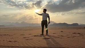 A person standing in a desert with a sunset in the background.