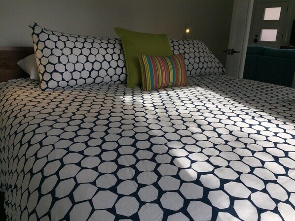 Un lit avec une couvre-lit à motifs et des oreillers, une porte avec une fenêtre, et une table de chevet avec une lampe.