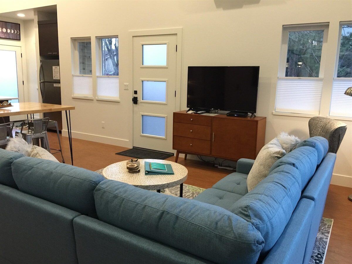 Un salon avec un canapé bleu, un téléviseur, un meuble en bois et un coin repas comprenant une table et des chaises.