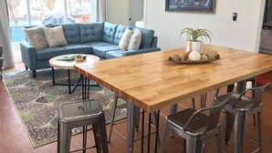 Un salon moderne avec un canapé d’angle bleu, une table à manger en bois avec quatre chaises et une grande fenêtre donnant sur l’extérieur.