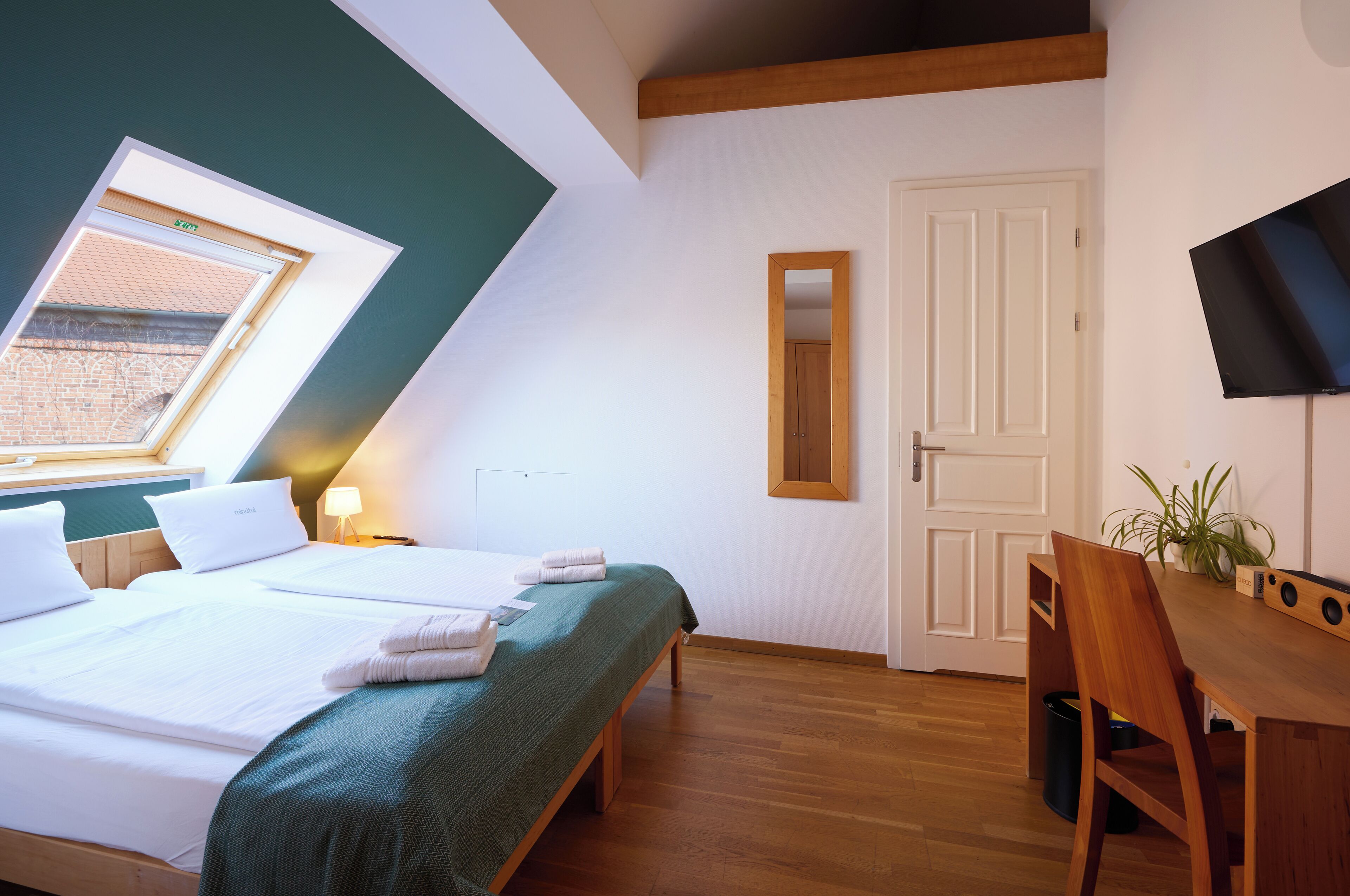 A hotel room with a bed, a desk, a chair, a TV, and a window with a view of a brick building.