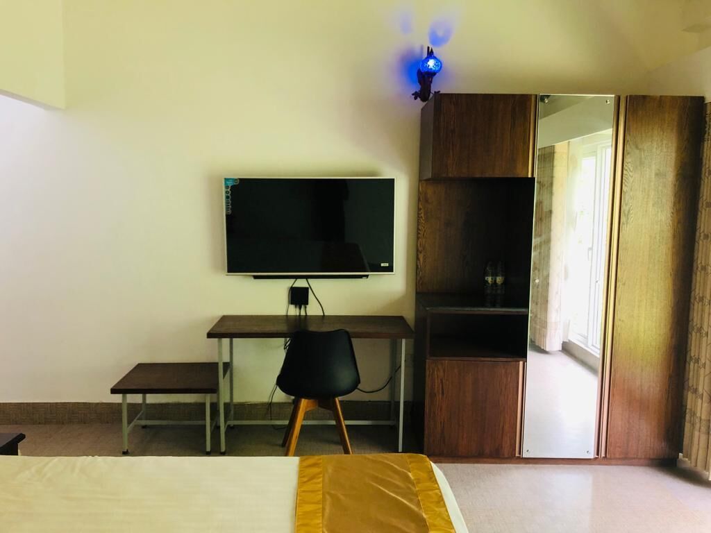 Un dormitorio con cama, escritorio con computadora, televisor y armario.