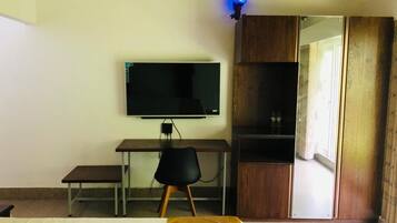 Un dormitorio con cama, escritorio con computadora, televisor y armario.