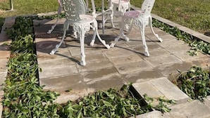 Un patio con una sombrilla roja, sillas de metal blancas y una mesa de piedra.