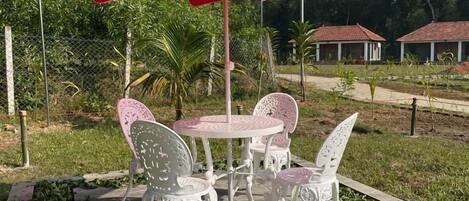 Een terras met een rode parasol, witte metalen stoelen en een stenen tafel.