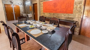 Un comedor con una larga mesa dispuesta para una comida, rodeada de sillas, con una pared de piedra y un letrero naranja grande arriba.