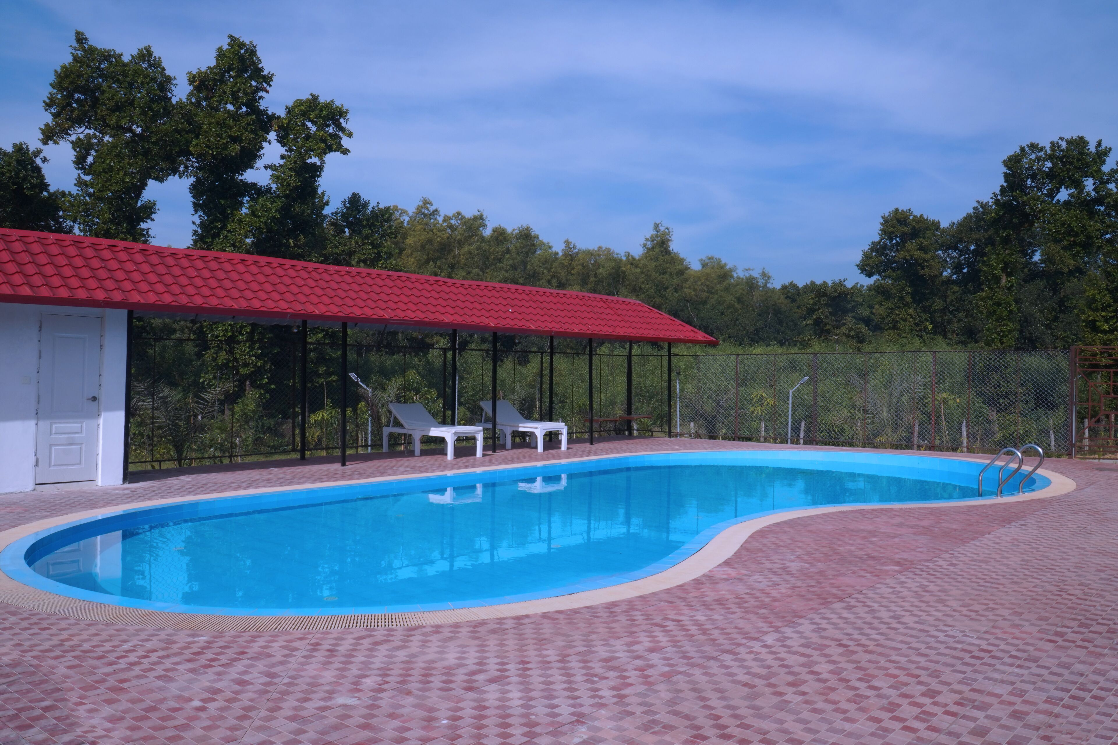 Ein Swimmingpool mit rotem Dach, umgeben von einem Zaun und zwei Liegestühlen.