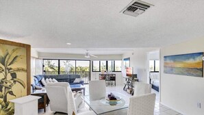 A spacious living area with a glass-top coffee table, white upholstered chairs, a blue sofa, and a large window offering a view of the outdoors. - Oceanfront Beautiful condo at a great location in Key Largo (Key Largo)