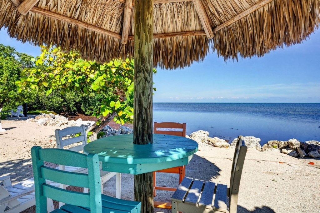 A beachside seating area with a thatched roof, a table, and chairs.