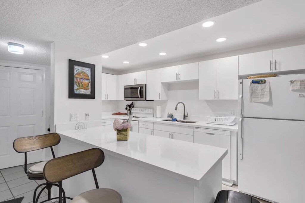 Una cocina moderna con armarios blancos, una isla central, un microondas y un refrigerador.