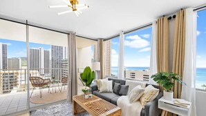 Ett modernt vardagsrum med en grå soffa, ett träbord och utsikt över stadsbilden och havet.