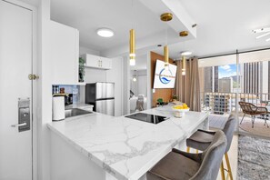 A modern kitchen with a marble countertop, stainless steel appliances, and pendant lighting.