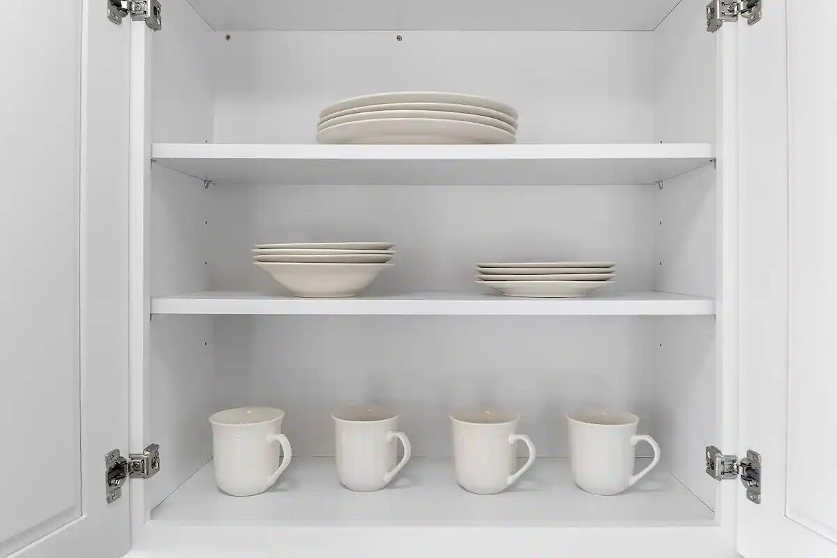A white cabinet with three shelves, each holding plates and cups.