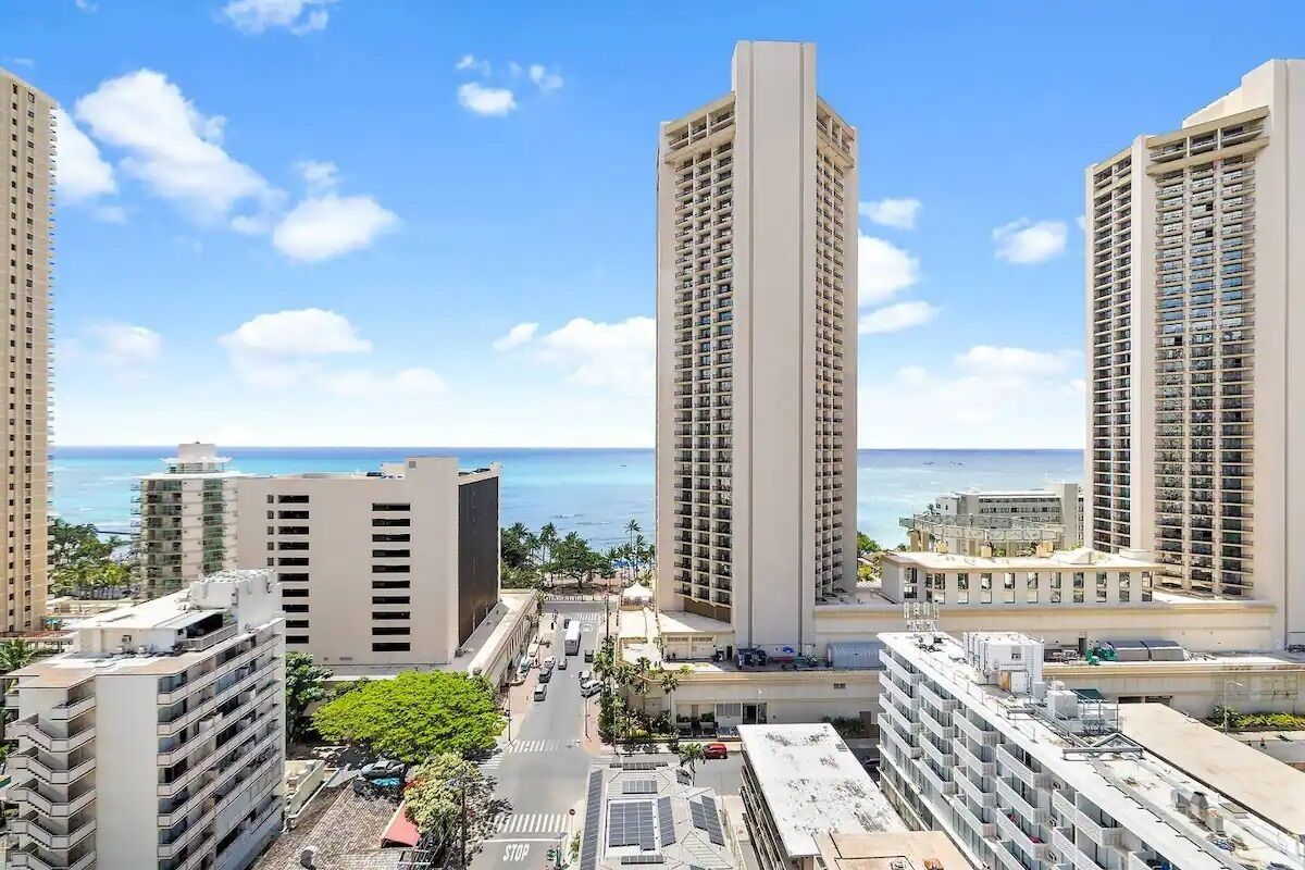 A high-rise hotel with multiple floors, a view of the ocean, and a clear sky.