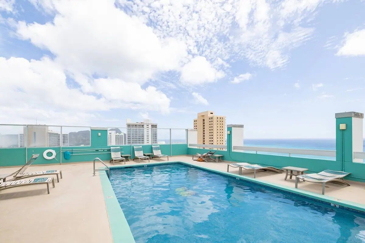 A rooftop pool with lounge chairs and a view of the city skyline.