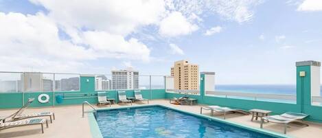 A rooftop pool with lounge chairs and a view of the city skyline.