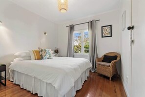Un dormitorio con cama, una silla, una ventana con cortinas, y una lámpara fijada a la pared.