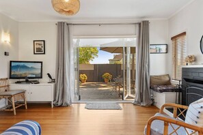 A living room with a television, seating area, and a view to an outdoor patio. - Otumoetai charmer beside the Mount (Tauranga)