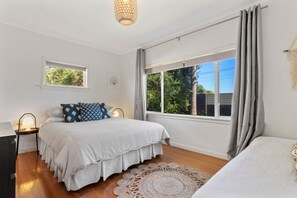 A bedroom with a bed, bedside lamps, a window with curtains, and a view of greenery outside.