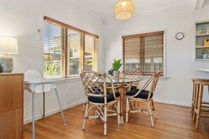 A dining area with a round table, four wicker chairs, and a hanging light fixture.