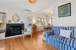 Ein Wohnzimmer mit Kamin, einem gestreiften Sofa, einem Essbereich mit Tisch und Stühlen sowie einer Küche im Hintergrund.