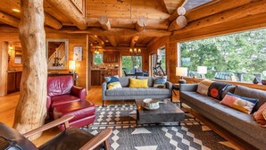 L’intérieur d’une cabane en rondins comprend un salon, un canapé en cuir rouge, un canapé gris et un coin repas.