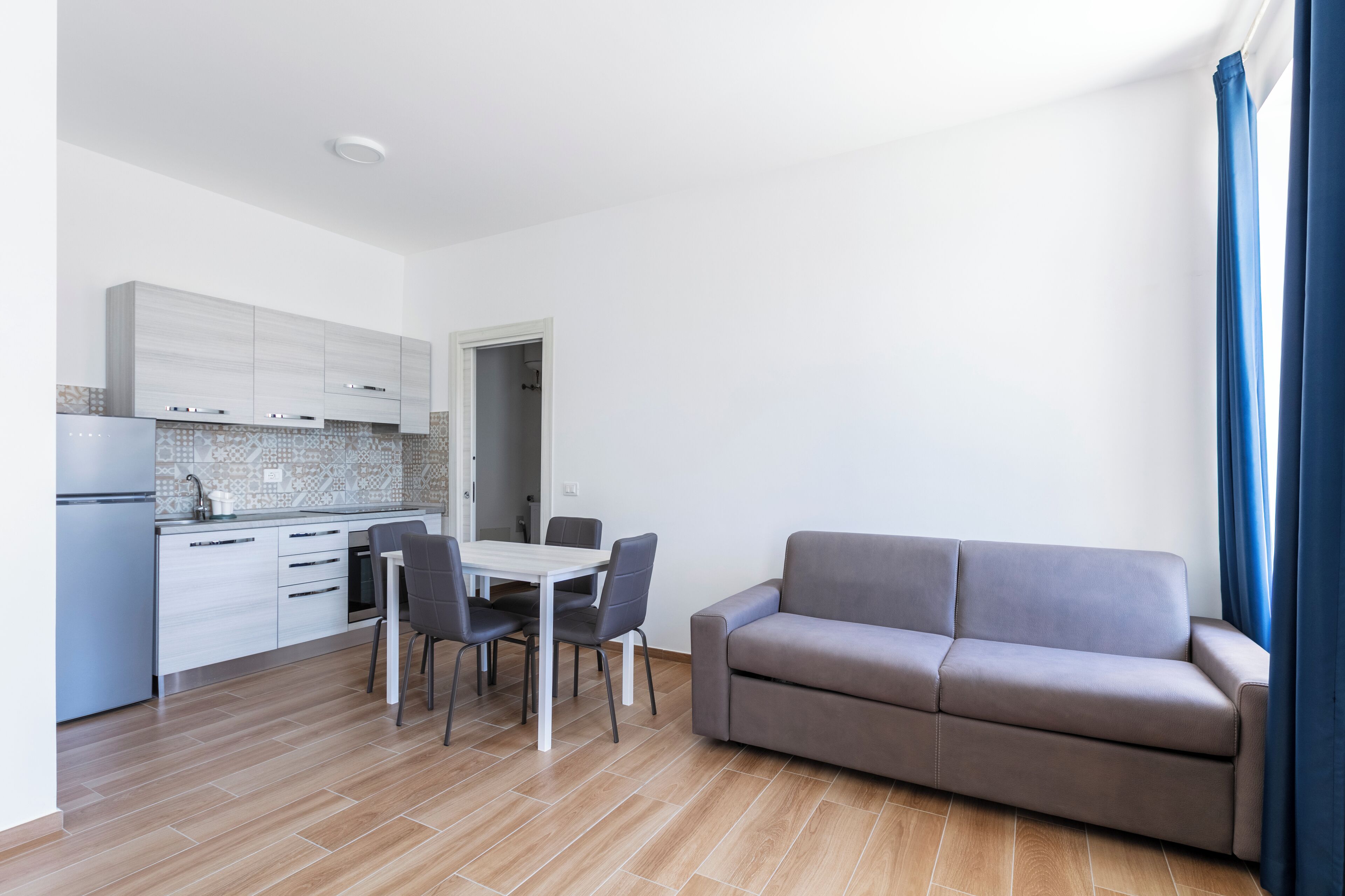 Eine moderne Küche mit weißen Schränken, einem Esstisch mit vier Stühlen und einem grauen Sofa.