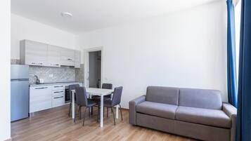 Eine moderne Küche mit weißen Schränken, einem Esstisch mit vier Stühlen und einem grauen Sofa.
