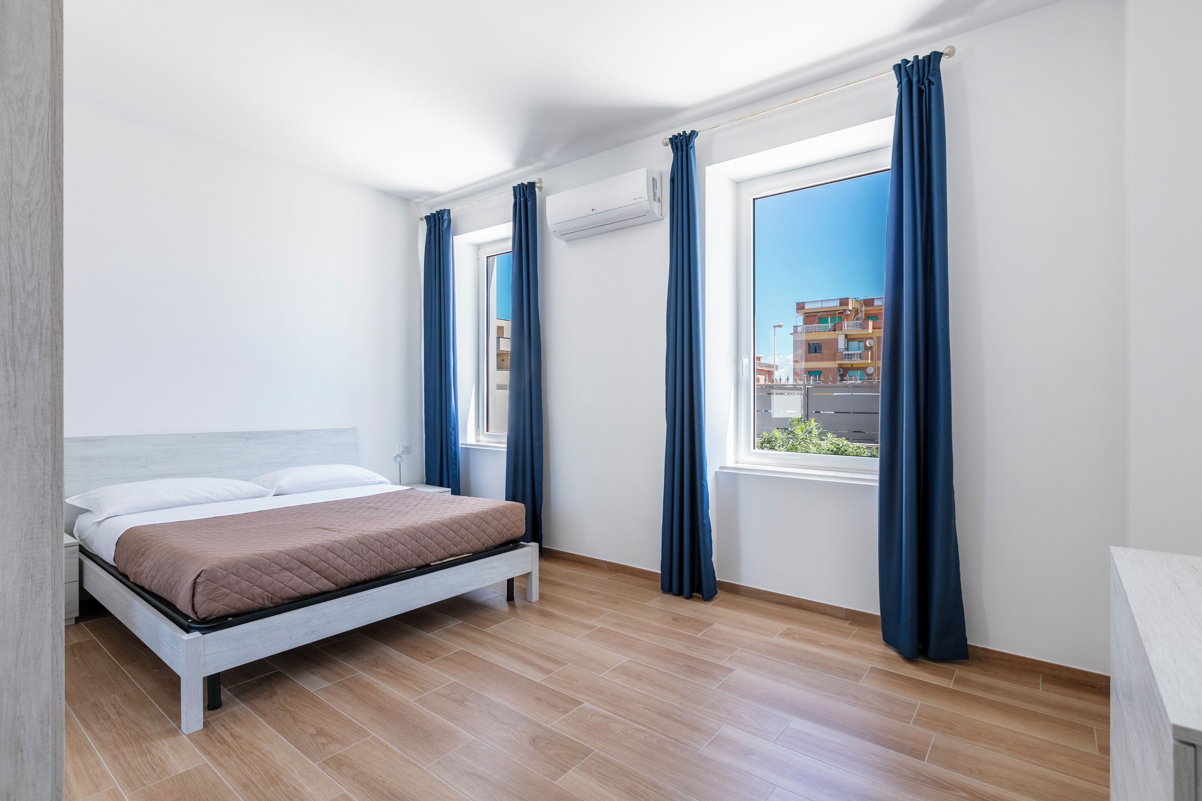 A bedroom with a bed, a nightstand, a window with curtains, and an air conditioning unit.