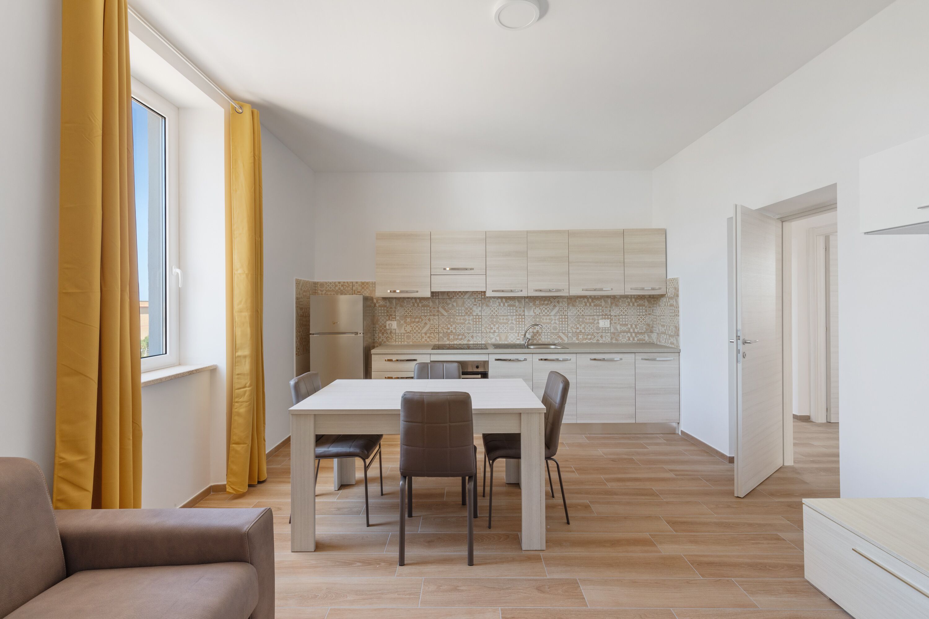 Una cocina moderna con armarios blancos, salpicadero de azulejos y comedor con mesa y sillas blancas.