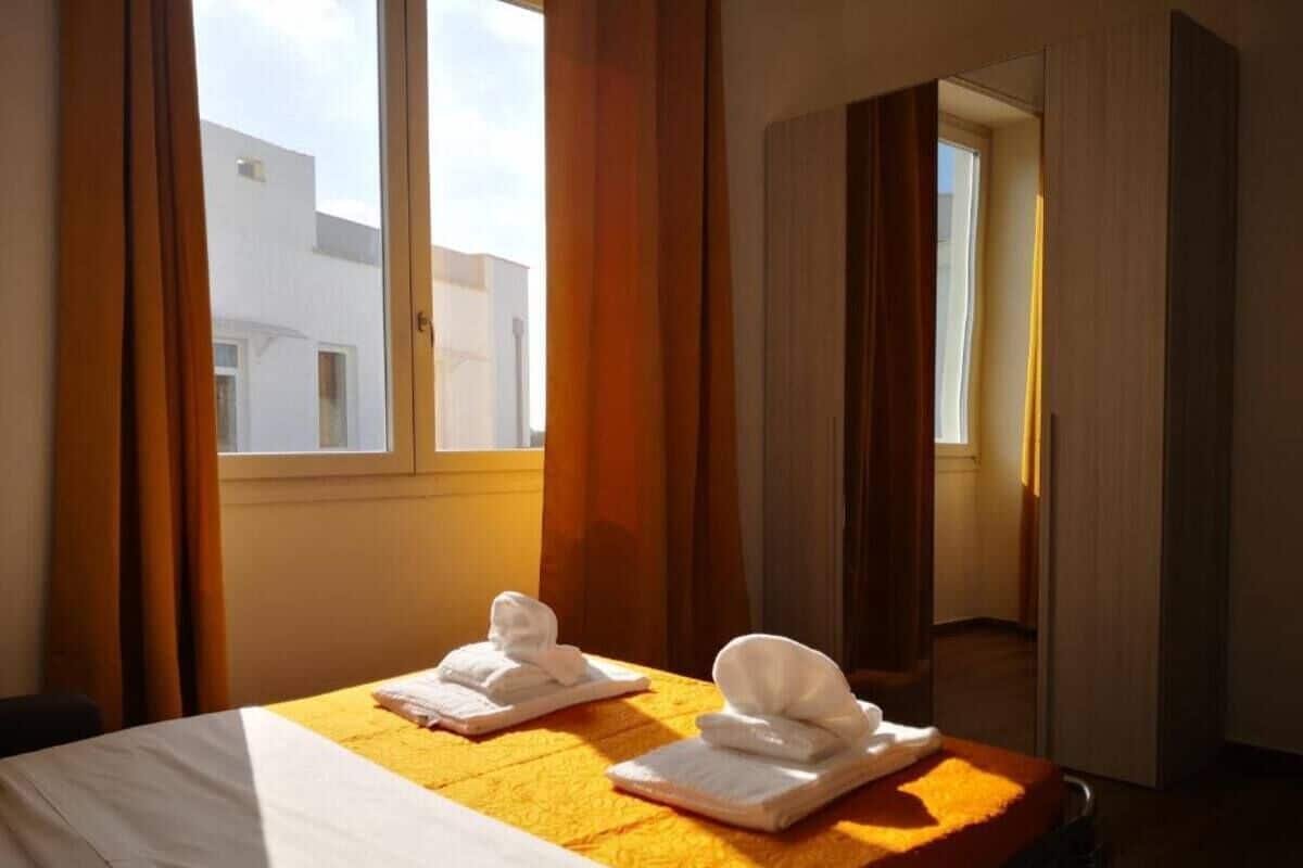 A hotel room with a bed, two towels, and a window with curtains.