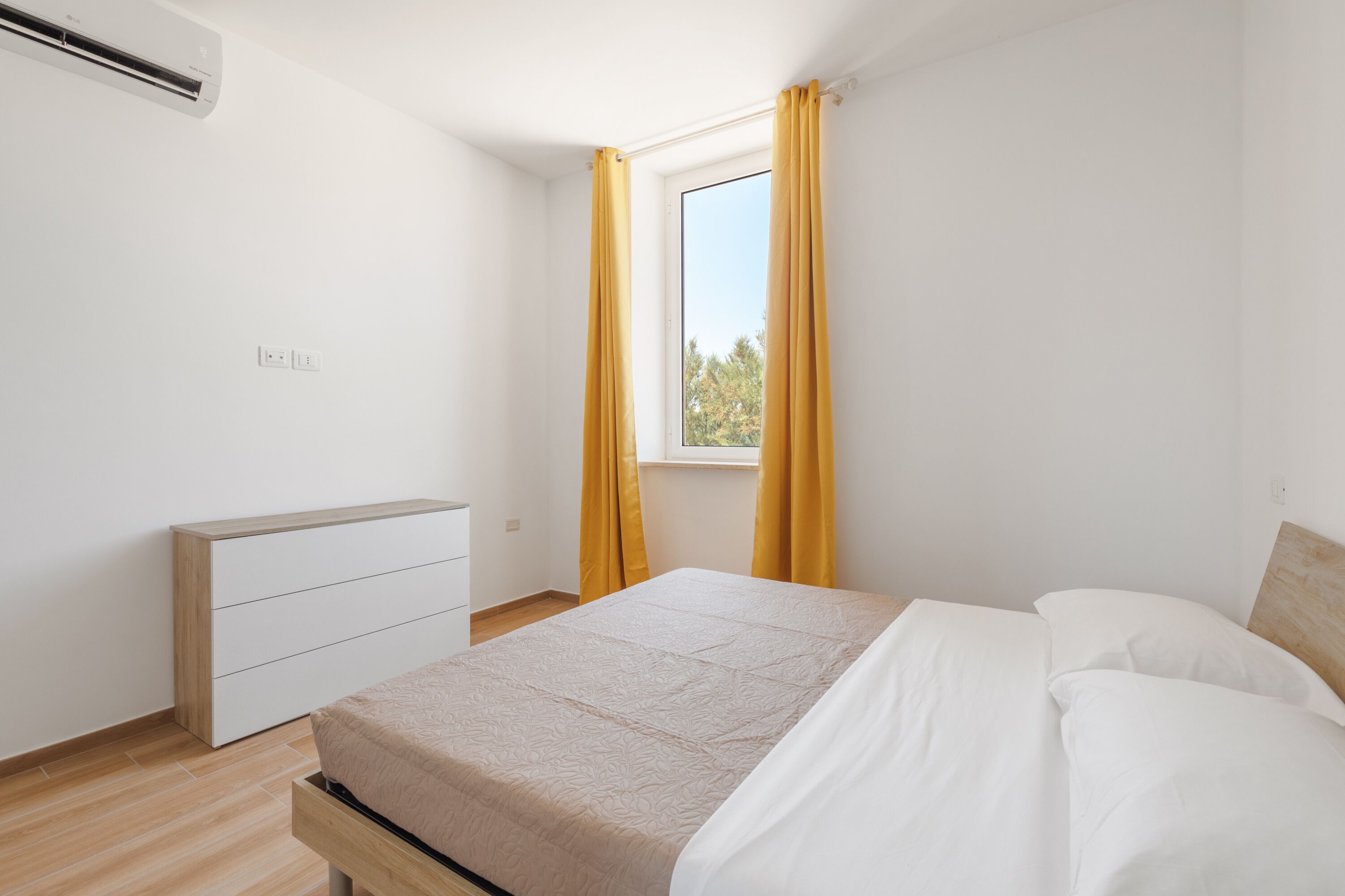 Een slaapkamer met een bed, een dressoir en een raam met gordijnen.