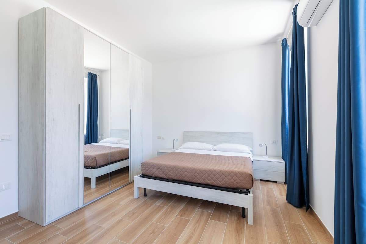 A bedroom with a bed, a wardrobe, a nightstand, and a mirror.